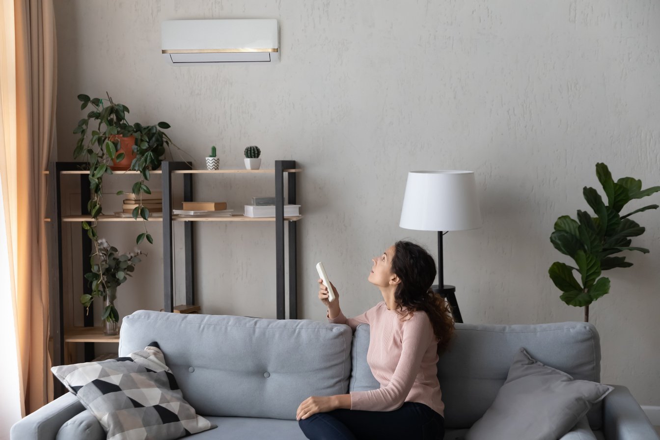 Woman sit on couch holding remote controller turns on airconditioner